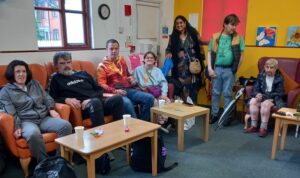 A group of people smiling, two standing and rest sitting in armchairs. They are in Bucks Mind's Sun House premises and are members of the Mind Gap Peer Support service.